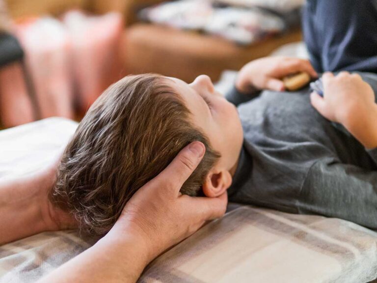 A mother helps her young son stretch before outdoor play on a sunny suburban lawn.