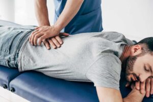 Adult receiving a gentle back assessment beside a spine model in a calm clinical room.